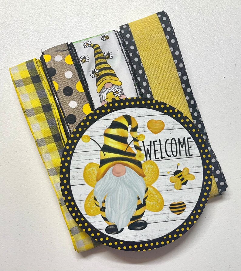 Op de afbeelding: Een set gele en zwarte gepatroneerde linten met een welkomstbord met een bijennom. Het bord heeft een witte achtergrond met zwarte stippen en het woord "WELCOME" in zwarte tekst.