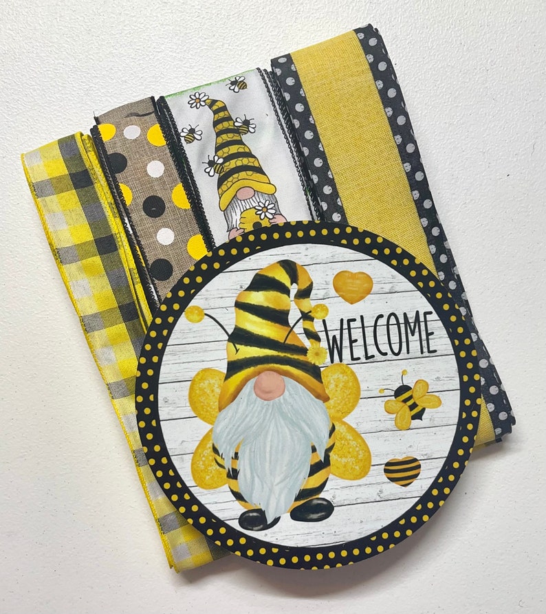 Op de afbeelding: Een set gele en zwarte gepatroneerde linten met een welkomstbord met een bijennom. Het bord heeft een witte achtergrond met zwarte stippen en het woord "WELCOME" in zwarte tekst.
