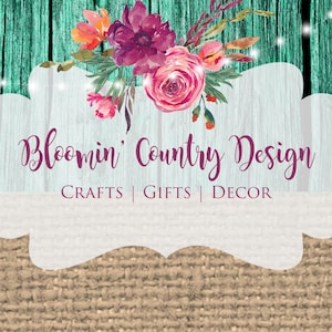 Op de afbeelding: Een wit bord met een bloemenontwerp en de tekst "Bloom'n Country Design" met de woorden "CRAFTS | GIFTS | DECOR" eronder. Het bord is op een rustieke houten achtergrond.