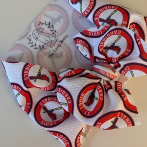 May include: White fabric headband with a red, white, and blue St. Louis Cardinals logo pattern. The headband is tied in a bow.