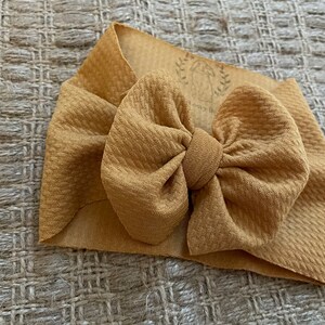 Könnte beinhalten: Ein gelbes Stoffhaarband mit einer großen Schleife. Das Haarband ist aus weichem, dehnbarem Material und perfekt, um jedem Outfit einen Hauch von Stil zu verleihen.