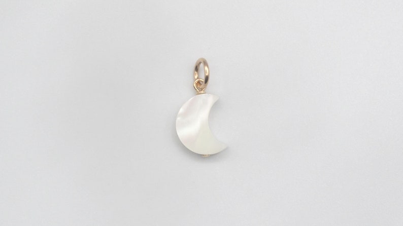May include: A gold charm in the shape of a crescent moon made of white mother of pearl.
