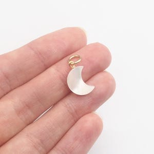 May include: A gold-tone crescent moon charm made of white mother of pearl. The charm is about 1 inch in size and has a loop for attaching to a necklace or bracelet.