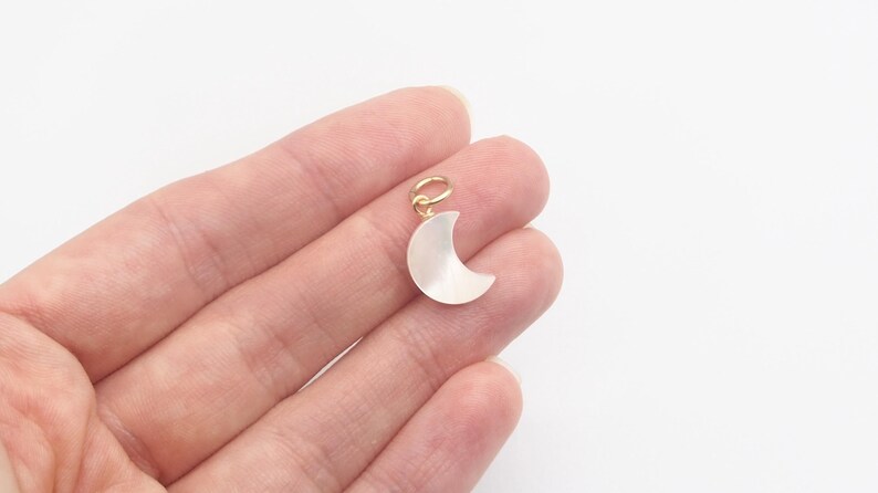 May include: A gold-tone crescent moon charm made of white mother of pearl. The charm is about 1 inch in size and has a loop for attaching to a necklace or bracelet.