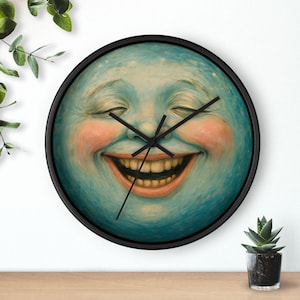 May include: A circular wall clock with a black frame. The clock face depicts a smiling moon face with closed eyes, rosy cheeks, and a wide grin. The clock hands are black.