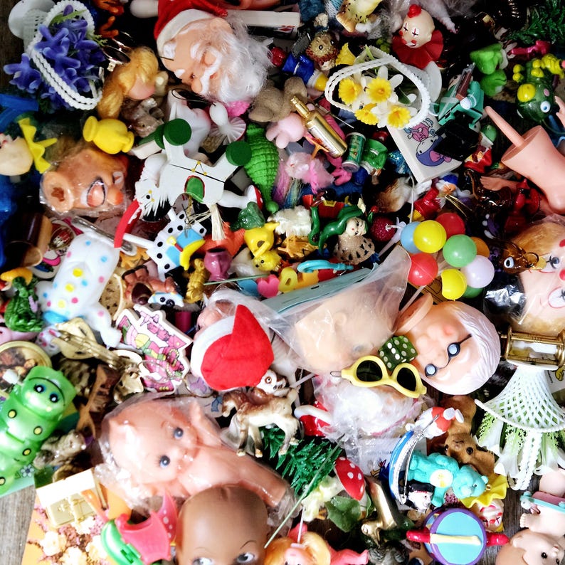 May include: A large collection of colorful plastic toys, including dolls, animals, and figures. There are also some small, decorative items, such as flowers and a bottle of wine.