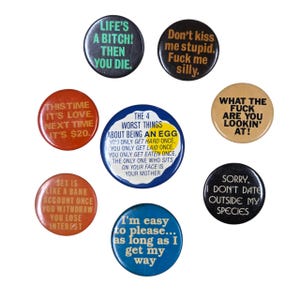Peut inclure: Ensemble de huit badges ronds avec des phrases audacieuses. Les badges sont de diff&eacute;rentes couleurs, dont le noir, le rouge, le bleu et le beige. Les textes sur les badges contiennent des phrases humoristiques et provocatrices.