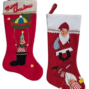 May include: Two red Christmas stockings with white tops. One features an elf in a hot air balloon with the text "Merry Christmas". The other has a Santa Claus design.