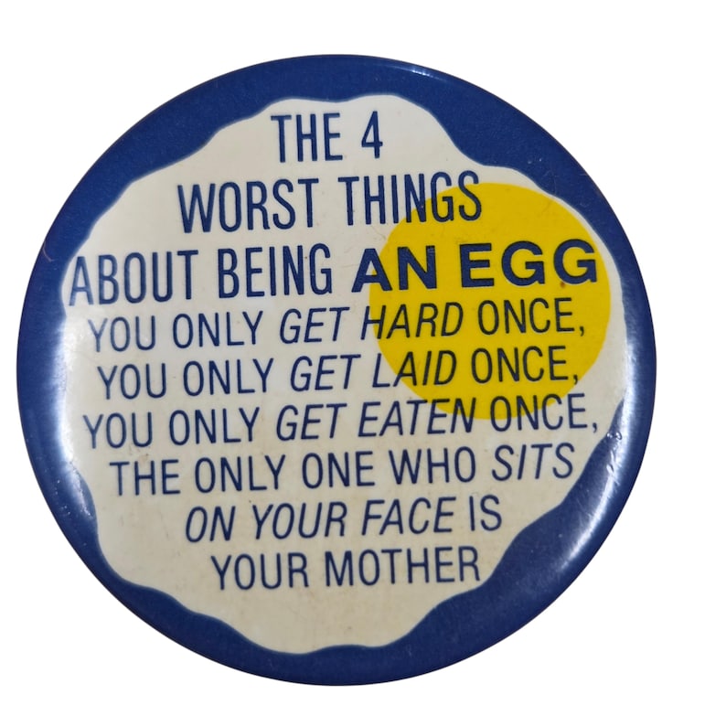 Peut inclure: Un bouton rond bleu avec le texte "THE 4 WORST THINGS ABOUT BEING AN EGG" et d'autres textes humoristiques. Le bouton a un design blanc en forme d'&oelig;uf avec un jaune d'&oelig;uf jaune.