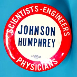 May include: A round political campaign button featuring a white center with the blue text JOHNSON HUMPHREY. A red border surrounds the center with the white text SCIENTISTS-ENGINEERS at the top and PHYSICIANS at the bottom, with a small emblem below the name.