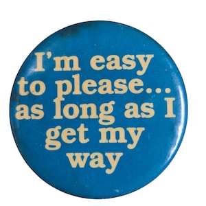 Peut inclure: Un bouton rond bleu avec le texte "I'm easy to please... as long as I get my way" en cr&egrave;me. Le bouton pr&eacute;sente une l&eacute;g&egrave;re usure.