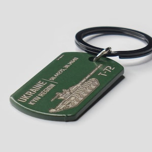 May include: Green metal keyring with a black metal ring. The keyring features a silhouette of a tank with the text "UKRAINE | KYIV REGION | 50.44275, 30.514640" and "T-72" on it.