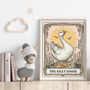 May include: A vintage-style illustration of a white goose with a yellow beak and blue eyes. The goose is standing on a green field with pink flowers and butterflies. The illustration is framed in a light brown frame with the text "The Silly Goose" at the bottom.