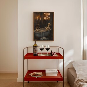 May include: A red serving cart with a bottle of wine, two wine glasses, and a bunch of grapes. A framed artwork depicts a skeleton relaxing in a bathtub with the text "Dying to Relax". The cart has two shelves and a metal frame.