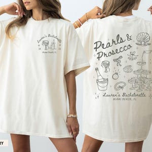 Può includere: Maglietta oversize color avorio con un design grafico sul retro che dice "Pearls & Prosecco" con una bottiglia di champagne, bicchieri e una collana di perle. Il davanti della maglietta dice "Lauren's Bachelorette" con una data e una località.