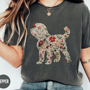 May include: A dark grey t-shirt featuring an embroidered floral design of a dog. The dog is outlined in white and filled with colourful flowers.