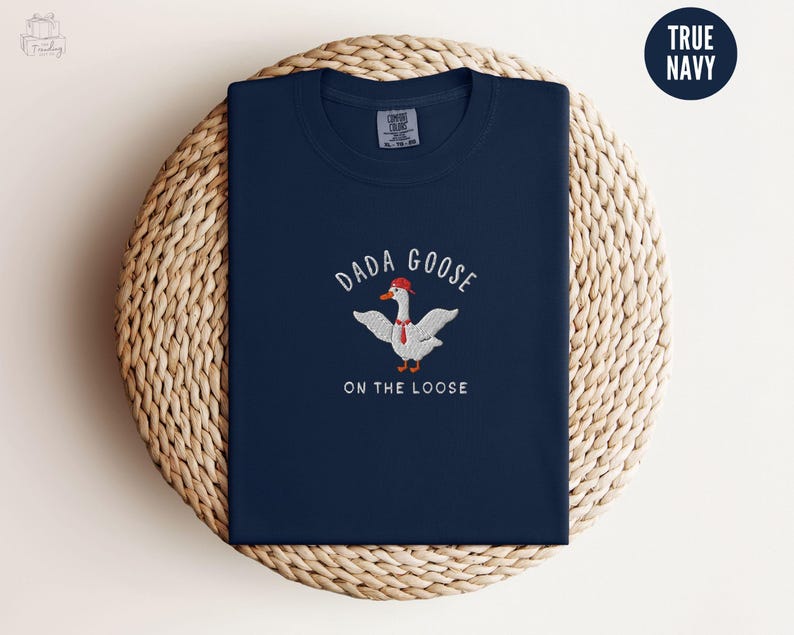 May include: A navy blue t-shirt with a white embroidered goose wearing a red hat and the text "Dada Goose on the Loose".