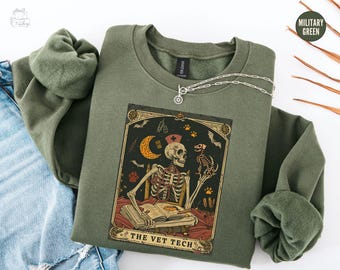 May include: A green sweatshirt with a vintage-style illustration of a skeleton wearing a nurse's cap and holding a small dog. The illustration is surrounded by a decorative frame and the text "The Vet Tech".