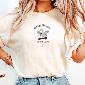 May include: A white t-shirt with the text "God's Silliest Goose On The Loose" and an embroidered image of a goose riding a scooter.