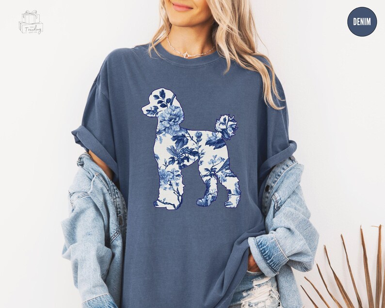 May include: A blue t-shirt with a white floral poodle silhouette design. The shirt is made of a soft, comfortable fabric and has a relaxed fit.