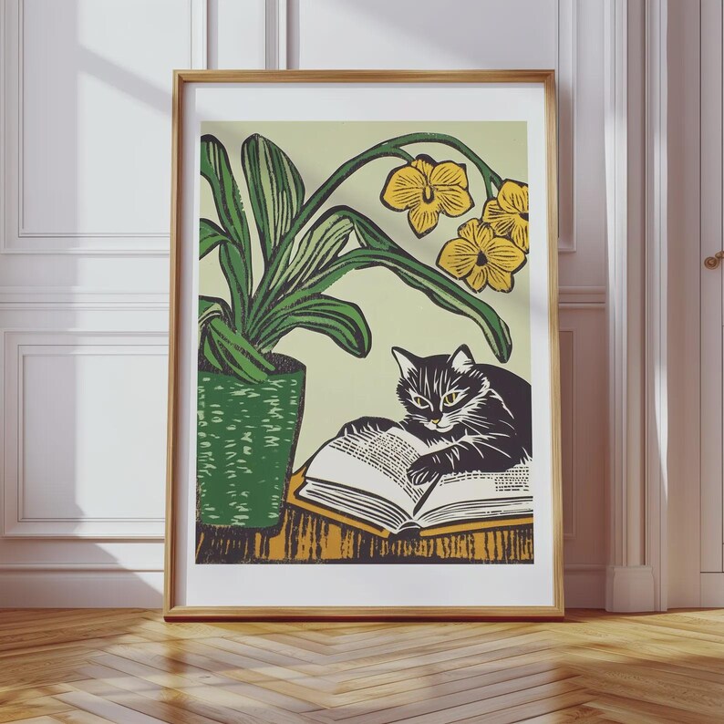 May include: A black and white cat sits on a table with a book open in front of it. The cat is looking at the book. There is a green potted plant with yellow flowers behind the cat.