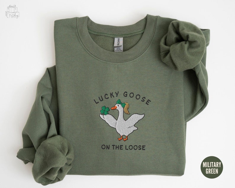 May include: A green sweatshirt with the text "Lucky Goose on the Loose" and an embroidered image of a goose wearing a hat and holding a four-leaf clover.