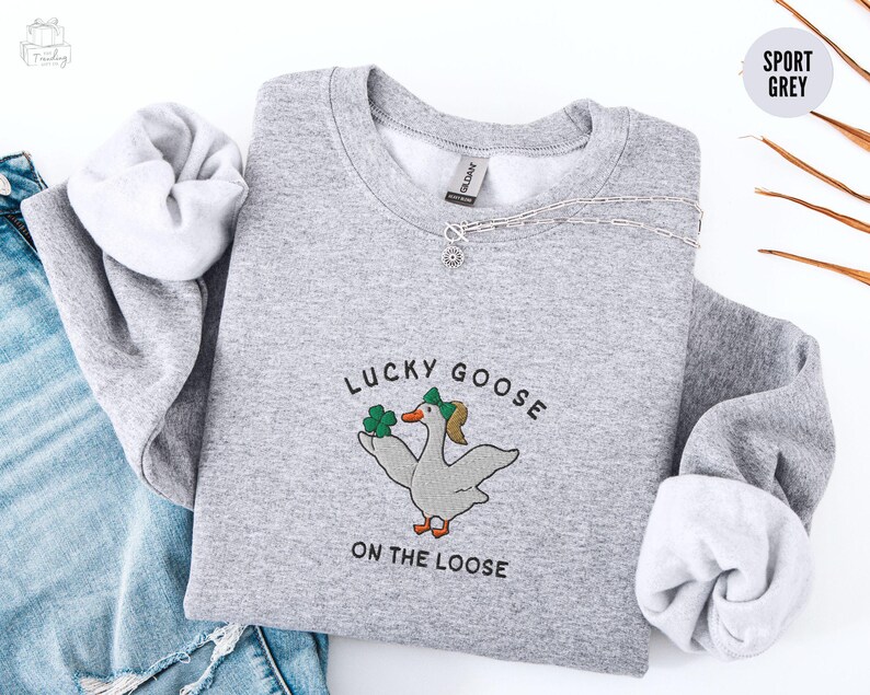 May include: A gray sweatshirt with the text "Lucky Goose on the Loose" and a cartoon goose wearing a green hat and holding a shamrock.