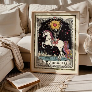 Puede incluir: Una ilustraci&oacute;n de carta de tarot con un esqueleto montando un unicornio arco&iacute;ris. La carta est&aacute; enmarcada en un marco de madera y tiene el texto "The Audacity" en la parte inferior.