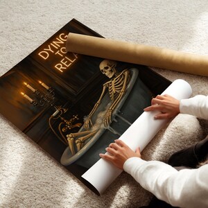 May include: A canvas print featuring a skeleton relaxing in a bathtub, with the words "Dying to Relax" in neon. The artwork includes a candelabra and a vintage bathtub. Two rolled-up posters are next to the print.
