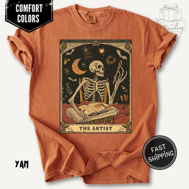 Puede incluir: Camiseta naranja quemado con un gr&aacute;fico estilo tarot de un artista esqueleto. El esqueleto sostiene un pincel y est&aacute; sentado frente a un libro abierto. El gr&aacute;fico incluye una luna creciente, una paleta y el texto "THE ARTIST".