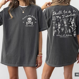 Könnte beinhalten: Dunkelgraues T-Shirt mit weißem Grafiktext und Illustrationen. Die Vorderseite zeigt ein Totenkopf- und gekreuzte Knochen-Design mit dem Text "Lauren's 30th Birthday, Miami Beach, FL." Auf der Rückseite steht "Death to My Twenties" mit Skelett-Illustrationen.