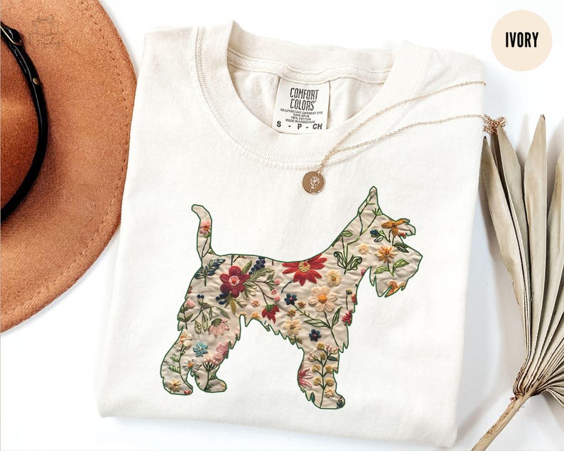 Puede incluir: Una camiseta blanca con un dise&ntilde;o floral en forma de perro. El dise&ntilde;o est&aacute; en tonos de rojo, rosa, amarillo y verde. La camiseta tiene una etiqueta que dice "Comfort Colors" y el texto "S - P - CH". La camiseta est&aacute; sobre un fondo blanco con un sombrero marr&oacute;n y una planta seca.