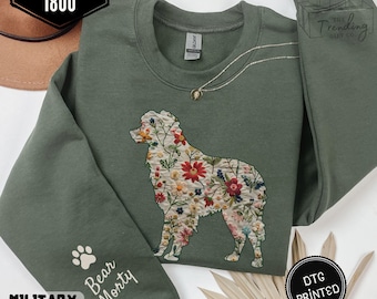 Puede incluir: Sudadera verde militar con un diseño floral de perro. La sudadera presenta el texto "Bear Morty" en la manga y "DTG Printed" en un círculo negro. También es visible la marca "Gildan 1800".