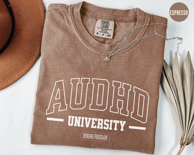 May include: A brown t-shirt with the text "ADHD University - Honors Program" in white. The shirt is a relaxed fit and has a distressed look.