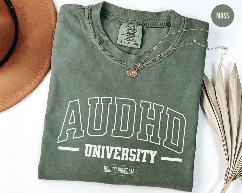 May include: A green t-shirt with the text "AUDHD UNIVERSITY - HONORS PROGRAM" in white. The shirt is made of a soft, comfortable material and has a vintage look.