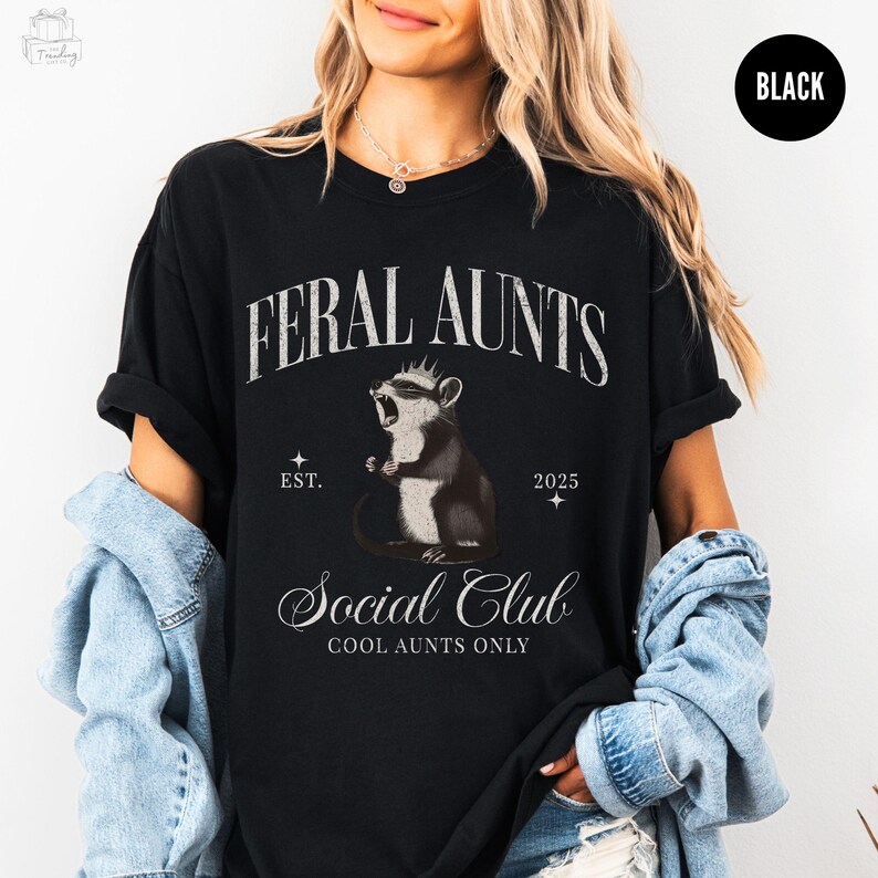 May include: Black t-shirt featuring a cartoon rodent graphic with the text "Feral Aunts Social Club Cool Aunts Only" and "Est. 2025"