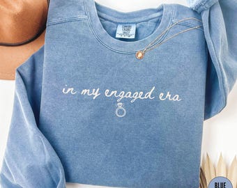 May include: Blue jean sweatshirt with the text "in my engaged era" and a small ring graphic.