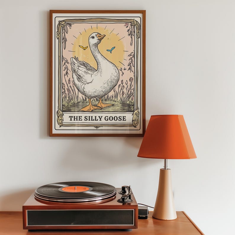 May include: A framed print of a white goose with a yellow beak and blue eyes. The goose is standing in a field of flowers and the print has the text "The Silly Goose" at the bottom.