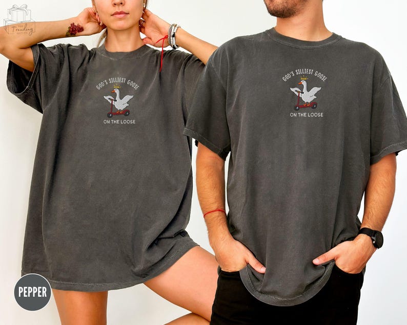 May include: A black t-shirt with a white goose wearing a crown riding a scooter. The text on the shirt reads "God's Silliest Goose On The Loose".