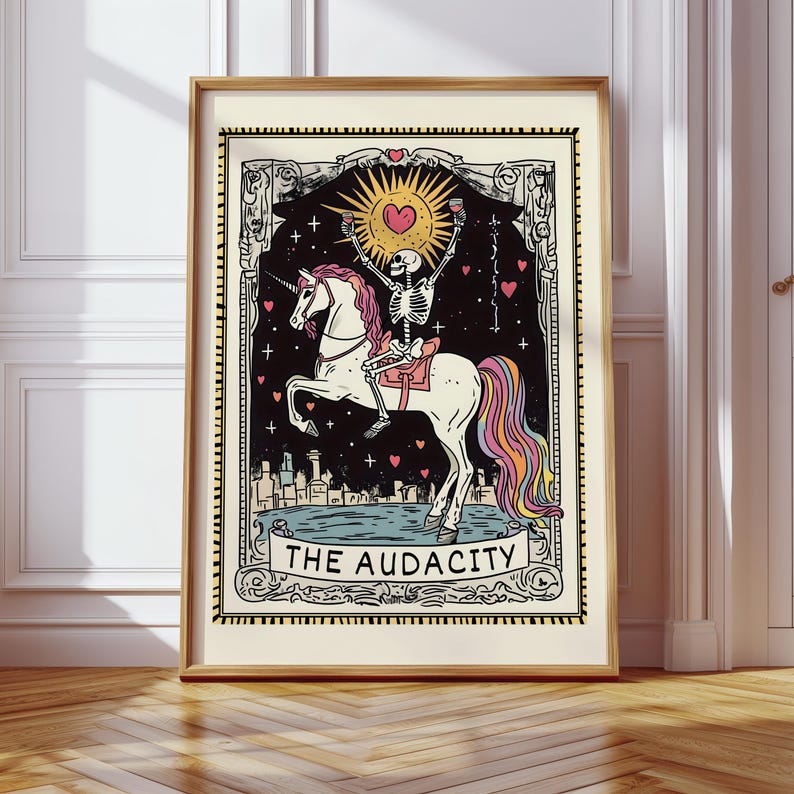 Puede incluir: Una ilustraci&oacute;n de carta de tarot con un esqueleto montando un unicornio con una crin de arco&iacute;ris. La carta est&aacute; sobre un fondo negro con estrellas y corazones. El texto "THE AUDACITY" est&aacute; impreso en una pancarta debajo del unicornio.