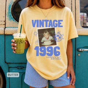 Puede incluir: Una camiseta de color amarillo pálido con el texto VINTAGE 1996 y LAUREN'S 30TH BIRTHDAY en azul. El gráfico incluye una foto cuadrada de una persona soplando velas en un pastel, rodeada de dibujos lineales azules de una bola de discoteca, estrellas y un pastel.
