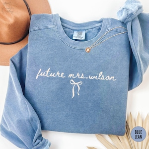 May include: A blue jean sweatshirt with the text "future mrs. wilson" in white lettering with a small white bow underneath.