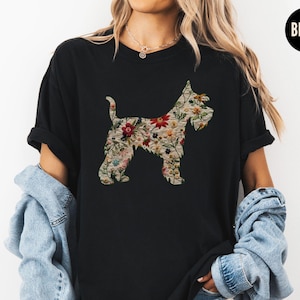 Puede incluir: Una camiseta negra con una silueta floral de un perro. El perro est&aacute; delineado con un patr&oacute;n floral de varios colores, incluyendo rosa, rojo, amarillo y verde.