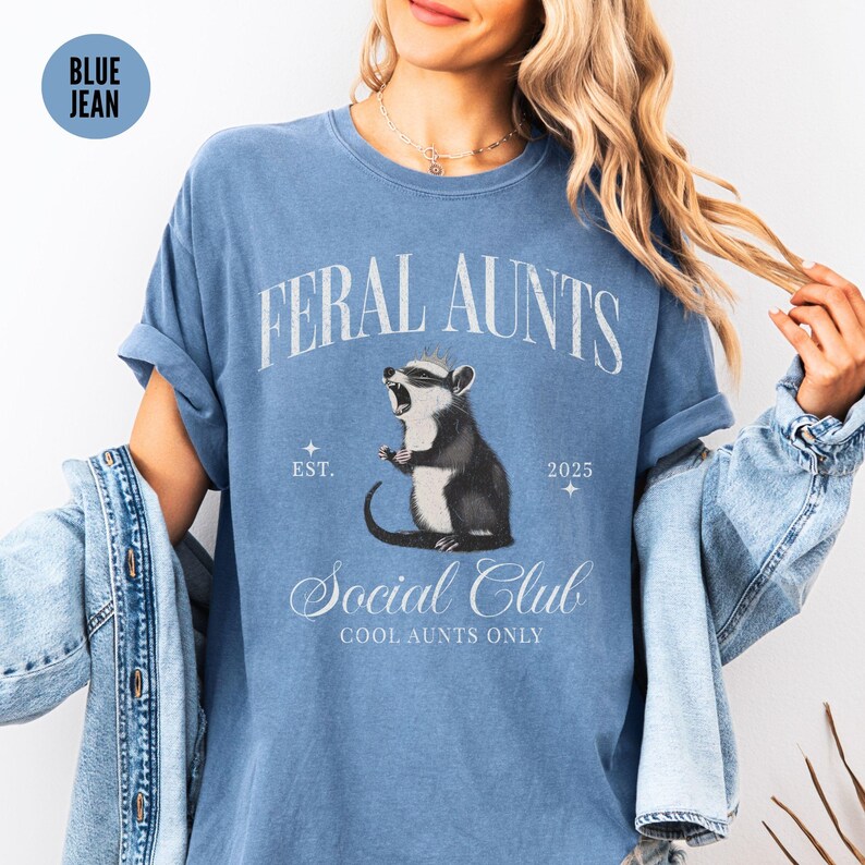 May include: A blue jean t-shirt with the text "Feral Aunts Social Club Cool Aunts Only" and a cartoon image of a rodent wearing a crown.