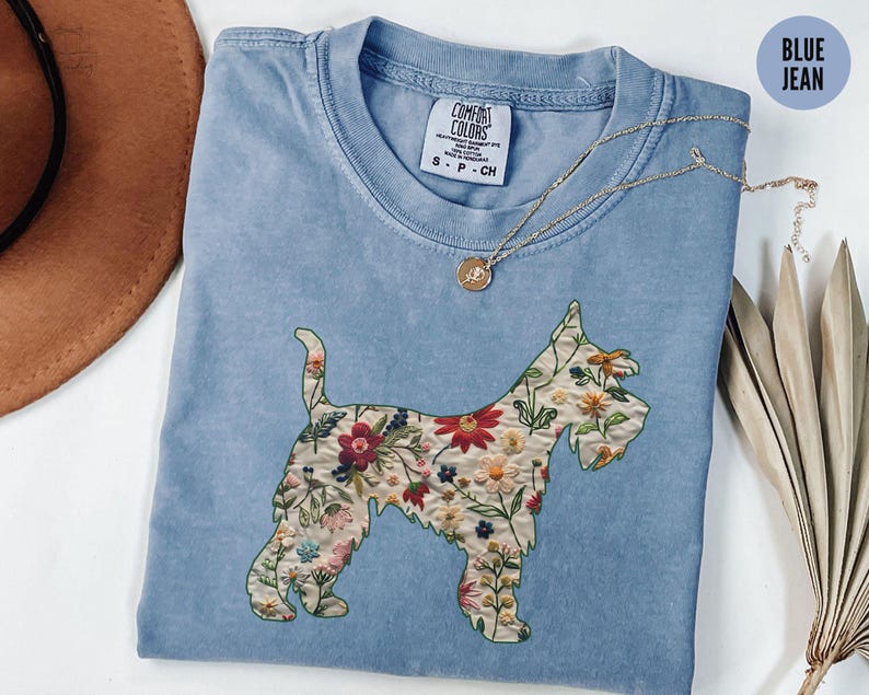 Puede incluir: Una camiseta azul claro con una silueta de perro bordada con flores. La camiseta tiene una etiqueta que dice "Comfort Colors" y "S-P-CH".