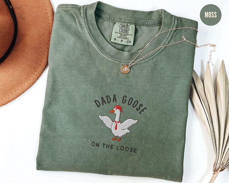 May include: A green t-shirt with the text "Dada Goose on the Loose" and an embroidered image of a goose wearing a red hat and a tie.