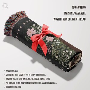 May include: A rolled up woven tapestry throw blanket with a floral pattern and the text "I'm so grateful for you". The blanket is tied with a red ribbon and has a fringe border. It is made of 100% cotton and is machine washable.