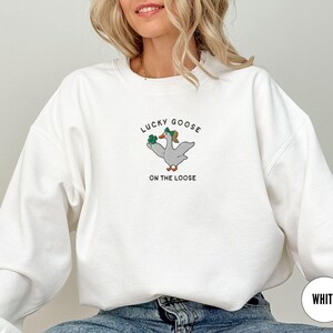 May include: White sweatshirt with a green shamrock and goose graphic and the text "Lucky Goose on the Loose".