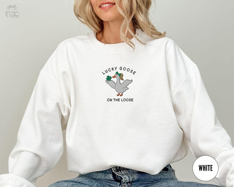 May include: White sweatshirt with a green shamrock and goose graphic and the text "Lucky Goose on the Loose".