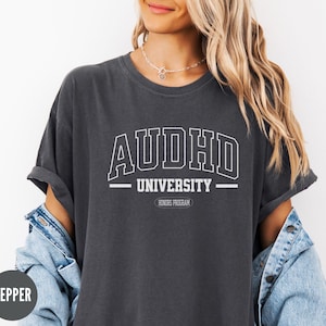 May include: A dark grey t-shirt with the text "AUDHD UNIVERSITY" in white. The text is in a collegiate font style with a banner underneath that reads "HONORS PROGRAM".